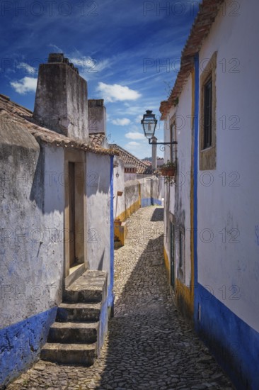Narrow streets of Obidos, Portugal, surrounded by white houses and blue accents on a sunny day