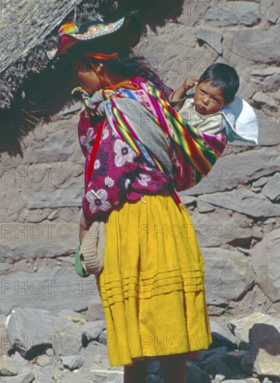 Young woman wearing traditional clothing carries her small child in a traditional way on Isla Taquile in Lake Titicaca, Andean Highlands, Peru, South America, September 1997, vintage, retro, old, historic