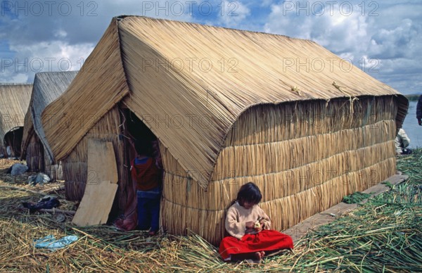 Little girl sitting in front of a reed hut on a floating Uro island in Lake Titcaca, Peru, South America, September 1997, vintage, retro, old, historic