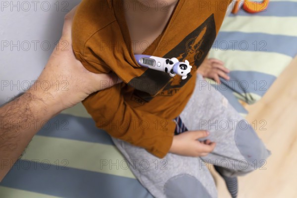 Parent's hand holding a crying child's arm with a digital thermometer placed under the armpit, accurately measuring body temperature while dealing with illness, fever, and flu