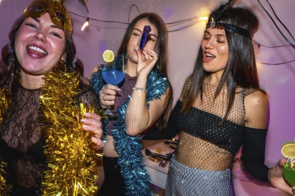 Young women in vibrant costumes laugh and clink cocktails at a festive new year's eve party indoors, celebrating friendship, glamour, and joyful togetherness late at night