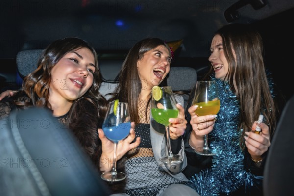 Three young women having fun traveling in a car at night, laughing and cheering with vibrant alcoholic drinks, celebrating friendship, special occasion, or a new year's eve party