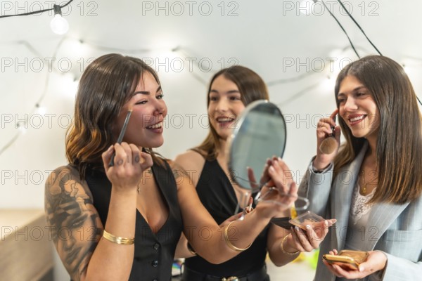Three young women, best friends, getting ready and applying makeup at home before a new year's eve celebration, sharing happy moments and beauty preparations