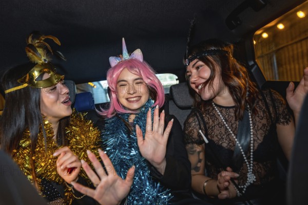 Three young women wearing festive costumes and garlands are happily laughing and dancing while safely traveling in the back seat of a car during a night celebration