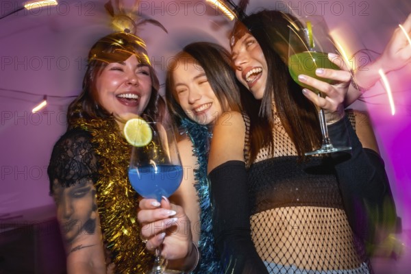 Three happy young adult women laughing while holding colorful cocktails, celebrating together with motion blur creating a dynamic, energetic atmosphere during a festive party