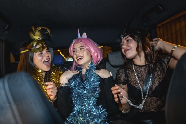 Three young women smiling, laughing, and having fun, dressed up in costumes with festive accessories, enjoying a lively party ride in the back seat of a car at night