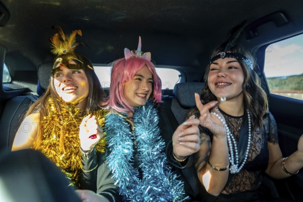 Three young women laughing and celebrating in a car back seat, wearing colorful tinsel boas and playful costume accessories for a festive night out or road trip party