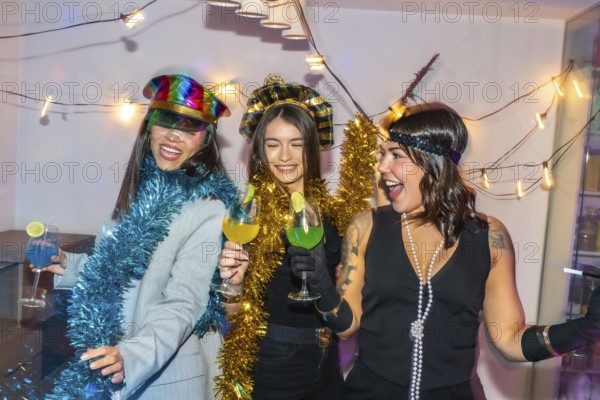 Three young diverse women smiling, laughing, and raising colorful cocktails, wearing festive costumes and tinsel garland during a new year's eve or themed party
