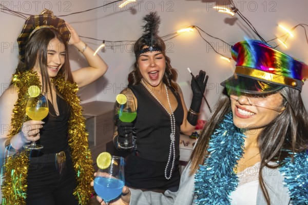 Young women friends celebrating new year's eve or a costume party indoors, laughing and dancing while holding colorful cocktails, surrounded by festive decorations and lights