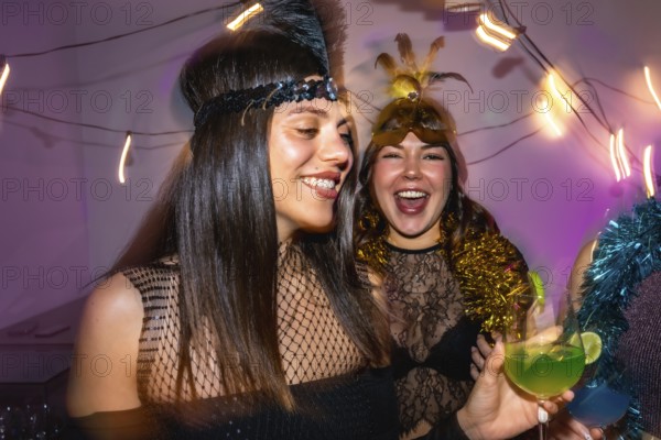 Joyful women wearing festive costumes and headbands, holding cocktails and laughing, enjoying a fun celebration together with string lights in the background