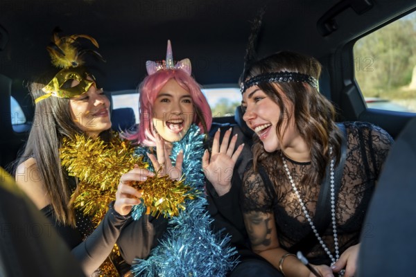 Happy young female friends wearing party costumes, tinsel garlands, and accessories, laughing and celebrating together in a car, enjoying a fun time and friendship