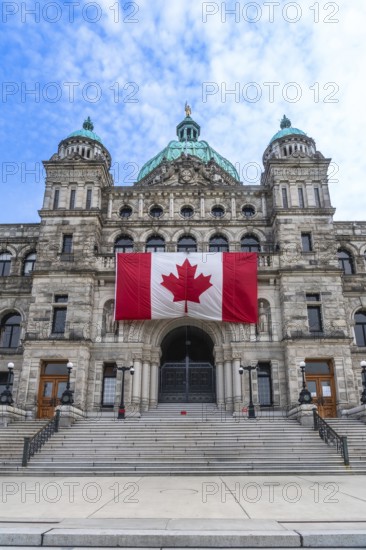 Large canadian flag hanging from the british columbia parliament buildings in victoria, british columbia, canada, on a bright summer day with blue sky and clouds