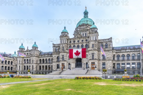 British columbia parliament buildings with large canadian flag hanging from the front during a sunny summer day in victoria, british columbia