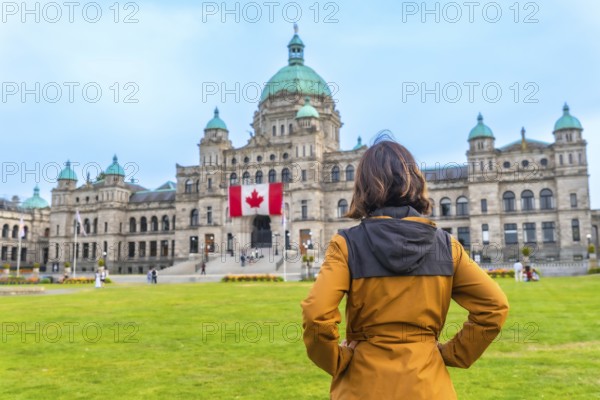 Tourist standing in front of the impressive parliament buildings, proudly displaying the canadian flag in victoria, british columbia, canada, on a bright, sunny summer day