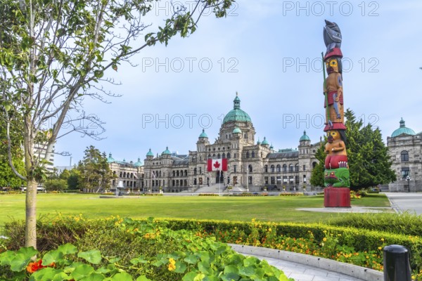 Canadian flag waving in the wind in front of the british columbia parliament buildings with a colorful totem pole in the foreground, located in victoria on vancouver island