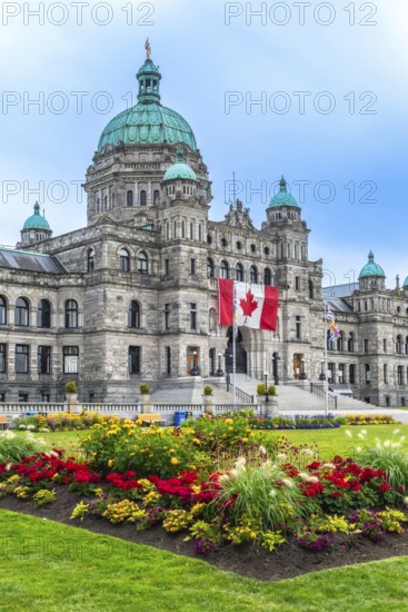 Canadian flag waving proudly in front of the british columbia parliament buildings in victoria, with colorful flowers adding vibrancy to the summer scene