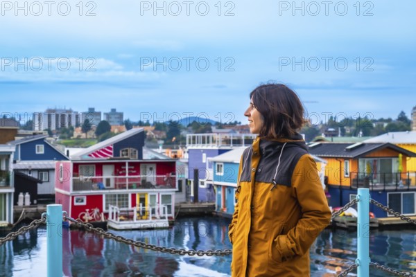 Young woman tourist admiring the colorful floating houses of fisherman's wharf park in victoria, british columbia, with the city skyline in the background under a summer sky