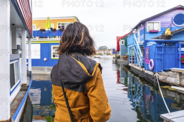 Tourist wearing a yellow jacket is enjoying the view of the colorful floating houses in fisherman's wharf park in victoria, british columbia, canada, a popular tourist destination