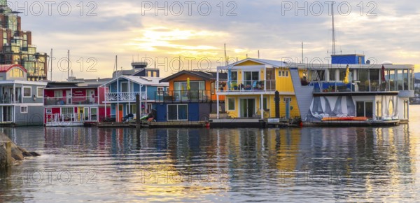 Colorful floating homes reflecting in the calm water at fisherman's wharf park in victoria, british columbia, create a picturesque scene during a vibrant sunset