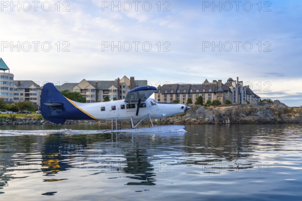 Seaplane taking off in the harbor of victoria, british columbia, with hotels and residential buildings along the waterfront in the background on a beautiful summer day