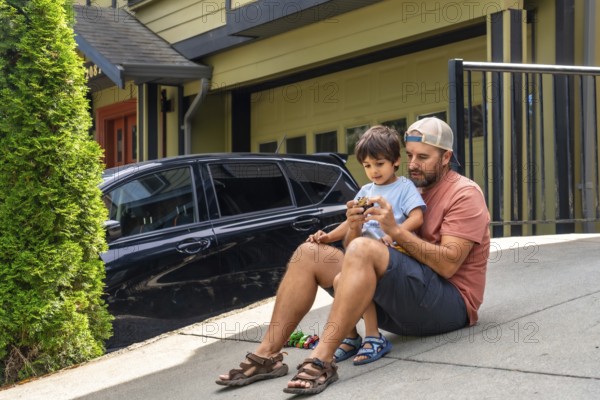 Father and son bonding while playing with a toy car on the driveway, sharing joyful moments together outside their home on a bright, sunny day filled with laughter and love
