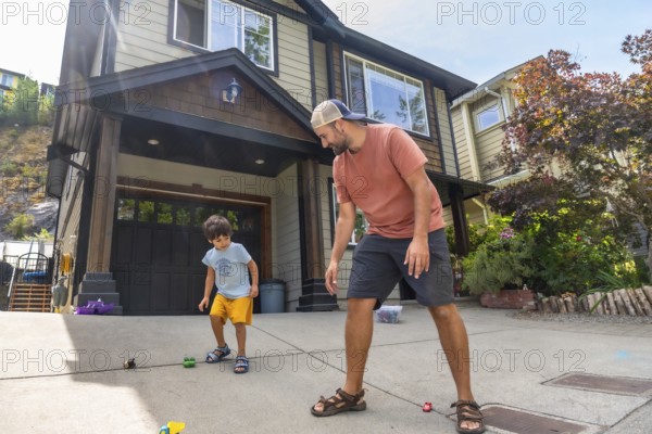 Father and son are bending down and playing with toy cars on the driveway of their house in canada during a sunny summer day, enjoying quality time together