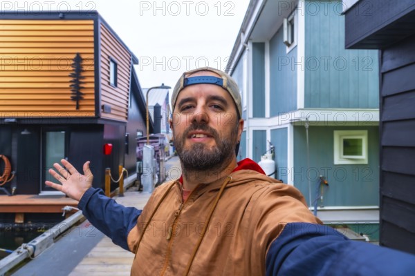 Tourist taking a selfie and showing with his hand floating houses in fishermans wharf park, victoria, british columbia, canada, in summer