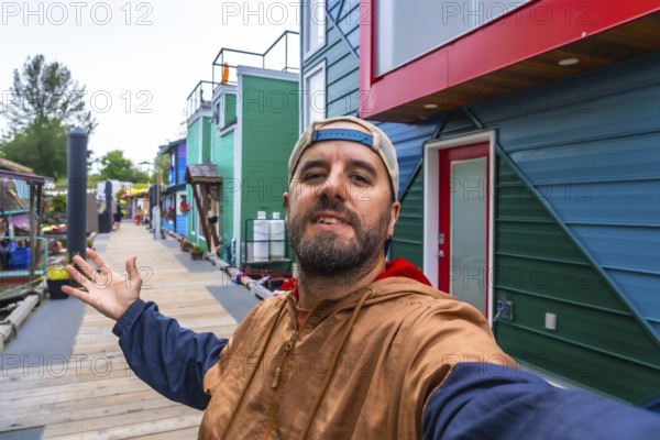 Tourist taking a selfie and showing colorful floating homes in fisherman's wharf park, a popular tourist destination in victoria, british columbia, canada