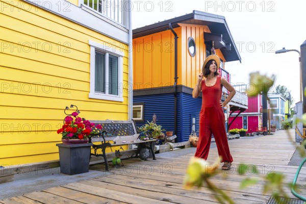 Tourist wearing jumpsuit and straw hat walking on wooden walkway in front of colorful floating houses in fisherman's wharf park in victoria, british columbia, canada during summer