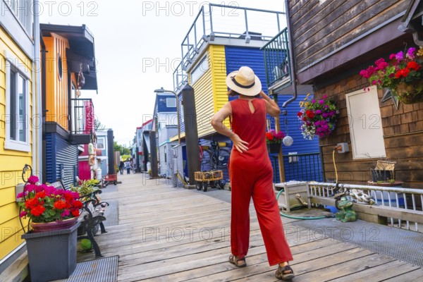 Tourist wearing a straw hat and a red jumpsuit walking in fisherman's wharf park, a colorful floating house community in victoria, british columbia, canada, during a sunny summer day