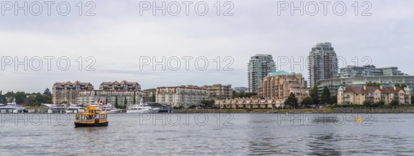 Yellow water taxi sailing in victoria, british columbia inner harbor with cityscape, condominiums, and moored boats in the background during a cloudy summer day