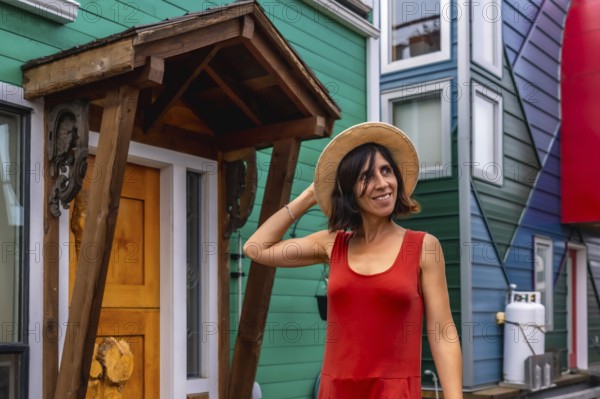 Smiling tourist holding her straw hat while visiting the colorful houses in the fisherman's wharf park, a popular and famous floating house community located in victoria, british columbia
