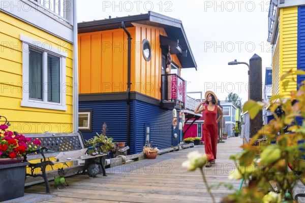 Tourist walking on a wooden walkway. Wearing a straw hat and a red jumpsuit. Exploring the colorful floating houses of fisherman's wharf park in victoria. British columbia. During a sunny summer day
