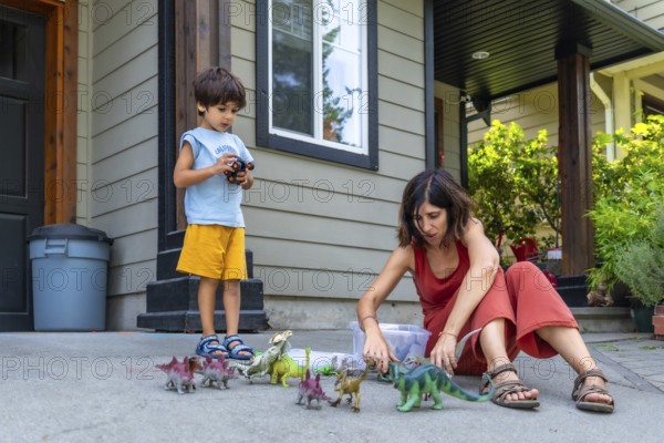 Mother and son enjoying quality time together, playing with dinosaur toys on the porch of their house, fostering imagination and creating joyful memories