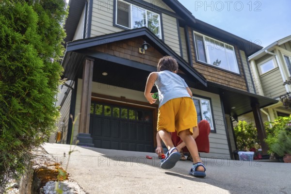 Two young brothers are happily playing with their toy cars on the driveway of their suburban home, enjoying a sunny day of outdoor fun and games