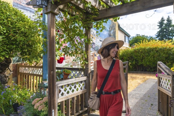 Smiling tourist in a straw hat and red jumpsuit walking out of a wooden gate in chemainus, a vibrant town known for its outdoor murals on a sunny summer day