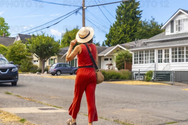 Tourist wearing a straw hat and red jumpsuit walking along a sunny sidewalk in chemainus, vancouver island, discovering the charming streets and houses of the town