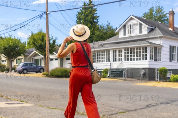 Female tourist wearing a straw hat and holding her hat while walking down a residential street in chemainus, british columbia, enjoying the summer weather and exploring the town