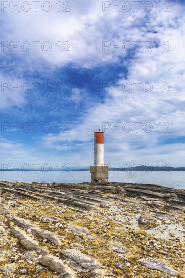 Red and white lighthouse standing on a rocky beach with a blue sky and clouds in the background in chemainus, vancouver island, british columbia, canada