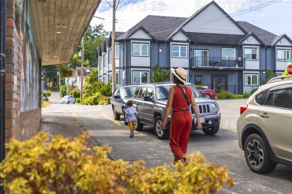 Mother and son enjoying a leisurely stroll along a charming sidewalk in chemainus, surrounded by colorful buildings and parked cars on vancouver island