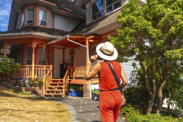 Female tourist wearing a straw hat and a red jumpsuit walking near a colorful wooden house in chemainus, vancouver island, british columbia, canada, during a sunny summer day