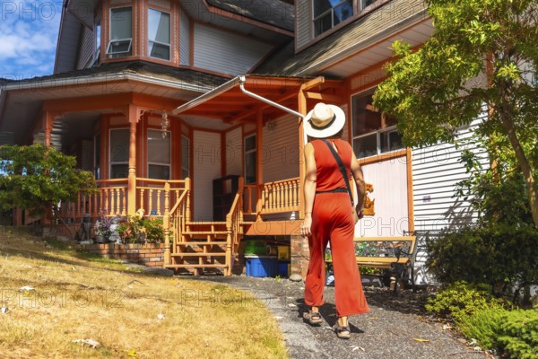 Tourist in a straw hat and red jumpsuit walking away from a colorful victorian house in chemainus, a vibrant art town on vancouver island, canada, on a sunny summer day