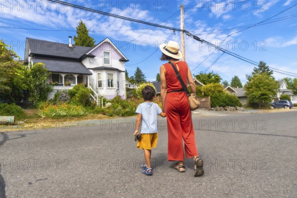 Tourist mother and son walking on a street in chemainus, vancouver island, british columbia, canada, admiring a typical house with a beautiful garden in summer