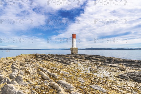 Red and white lighthouse rising from a rocky, textured coastline in chemainus, vancouver island, british columbia, canada, creating a picturesque maritime scene under a cloudy summer sky