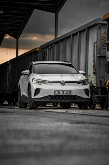 White car between freight cars at dusk, VW ID4 electric car, Deer Carsharing, Calw, Germany