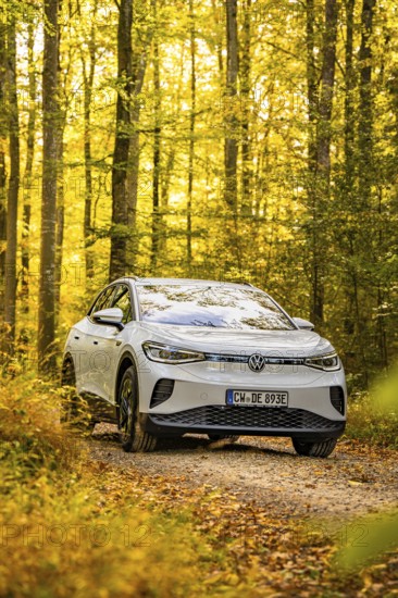An SUV drives on a forest path in autumn surrounded by yellow leaves under bright sunlight, VW ID4 electric car, deer car sharing, Calw, Germany