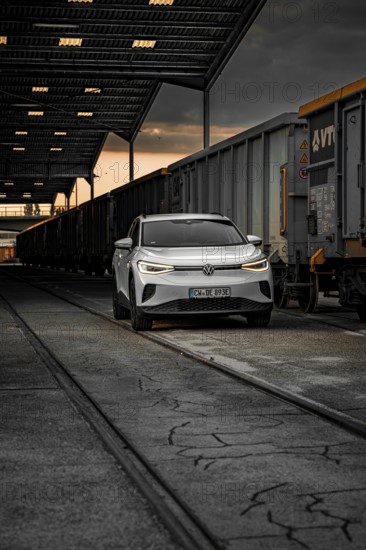 White car at night next to freight trains in depot, VW ID4 electric car, Deer Carsharing, Calw, Germany