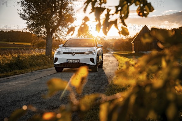 White car at sunset on the road with a farm in the background, VW ID4 electric car, Deer Carsharing, Calw, Germany