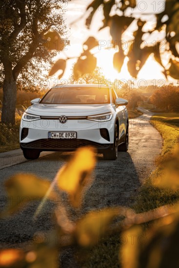 White car on a country road at sunset surrounded by leaves, VW ID4 electric car, Deer Carsharing, Calw, Germany