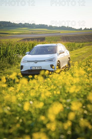 White car drives through a green field with yellow flowers in summer, VW ID4 electric car, Deer Carsharing, Calw, Germany